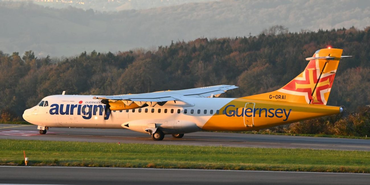 Aurigny Air Services plane on a runway at sunset with scenic hills in the background.
