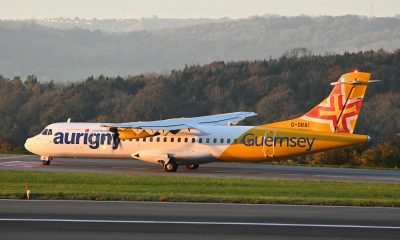 Aurigny Air Services plane on a runway at sunset with scenic hills in the background.