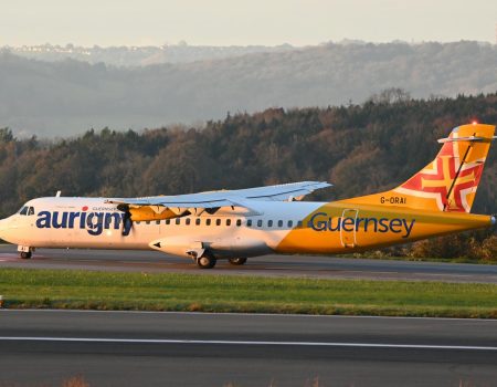 Aurigny Air Services plane on a runway at sunset with scenic hills in the background.