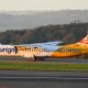 Aurigny Air Services plane on a runway at sunset with scenic hills in the background.