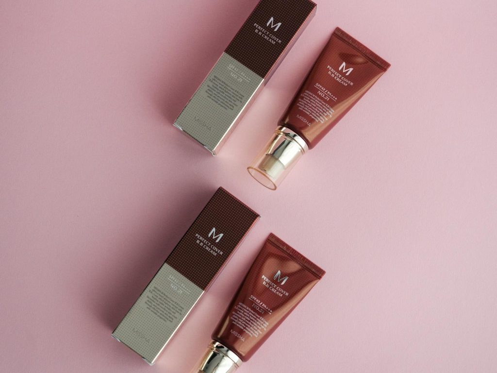 Flat lay of cosmetic products on a pink surface featuring foundation creams.