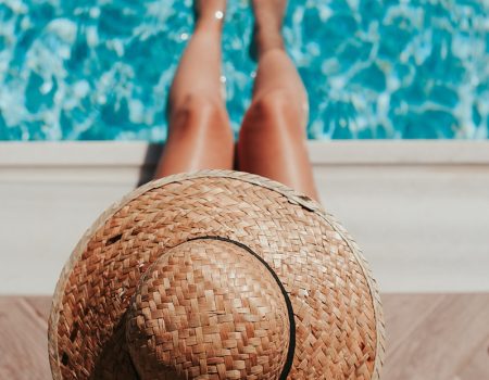 woman sitting on poolside setting both of her feet on pool