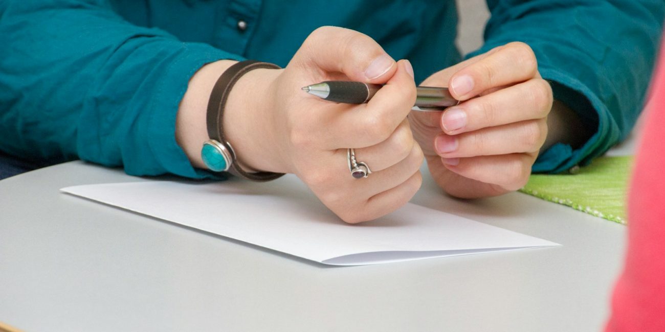 a person sitting at a table writing on a piece of paper