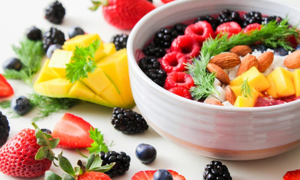 A vibrant bowl filled with fresh berries, mango, almonds, and herbs, perfect for a healthy snack or breakfast.