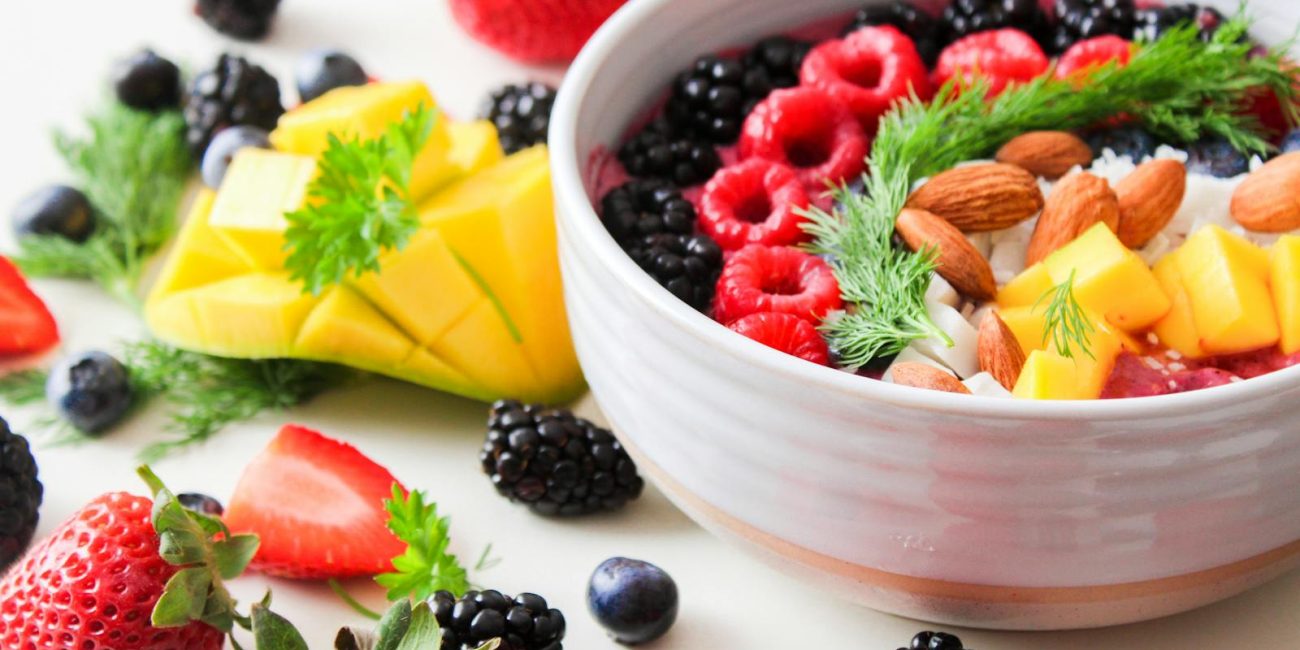A vibrant bowl filled with fresh berries, mango, almonds, and herbs, perfect for a healthy snack or breakfast.