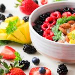 A vibrant bowl filled with fresh berries, mango, almonds, and herbs, perfect for a healthy snack or breakfast.