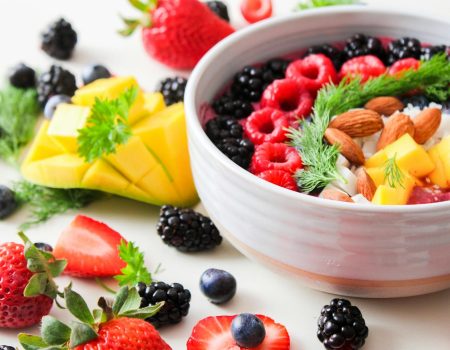 A vibrant bowl filled with fresh berries, mango, almonds, and herbs, perfect for a healthy snack or breakfast.