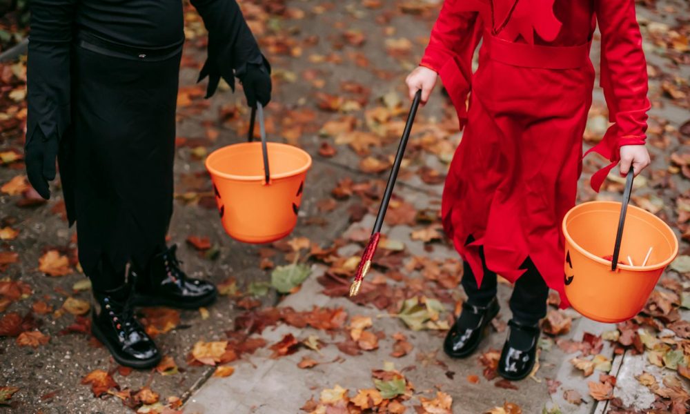 Two children in costumes holding Halloween buckets filled with candy.