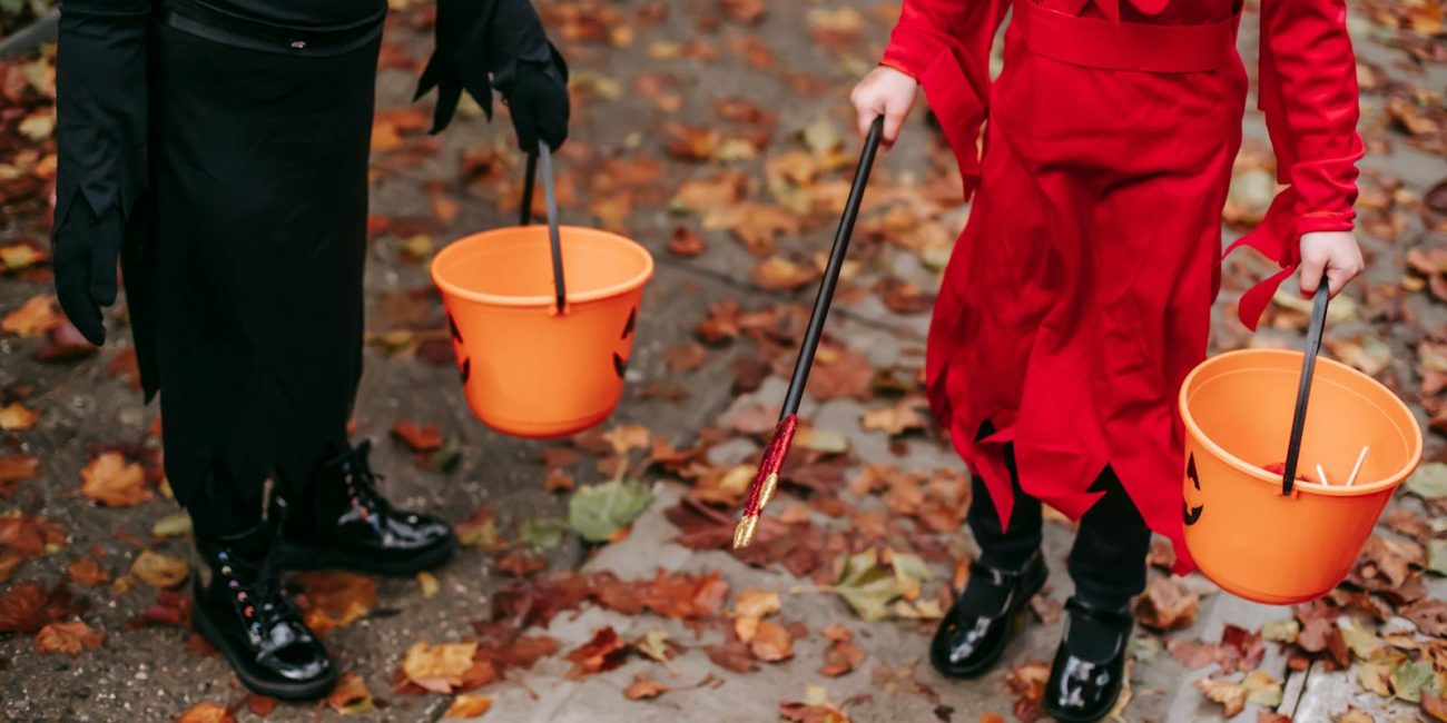 Two children in costumes holding Halloween buckets filled with candy.