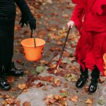 Two children in costumes holding Halloween buckets filled with candy.