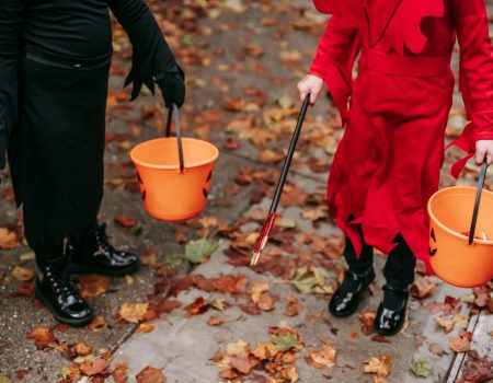 Two children in costumes holding Halloween buckets filled with candy.