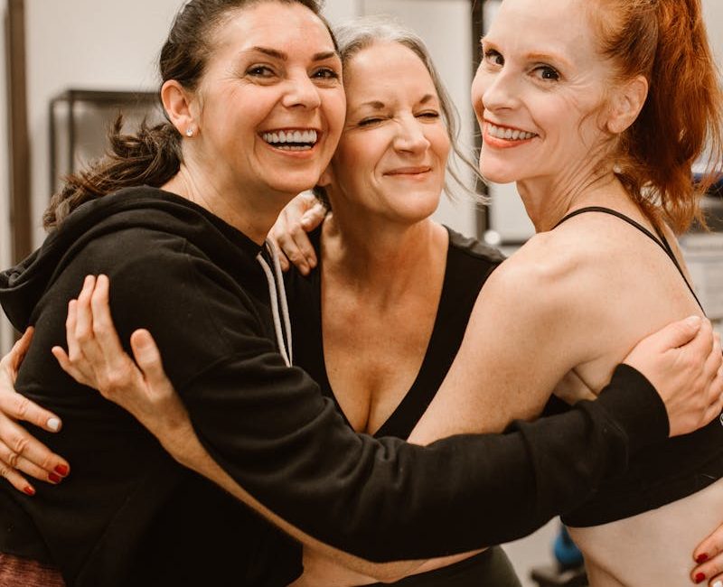 Three happy women hugging at the gym, celebrating friendship and wellness.