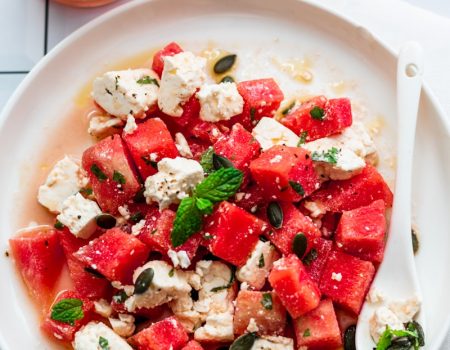 a plate of watermelon and feta salad next to a glass of water