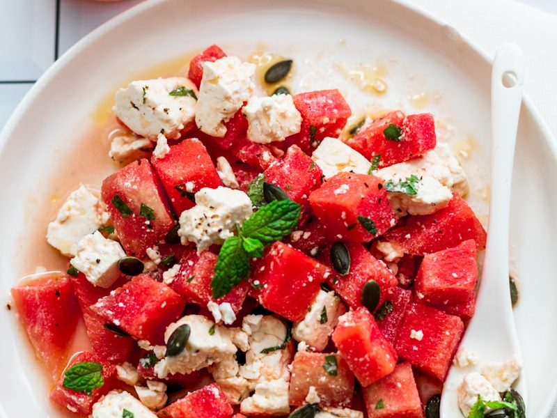 a plate of watermelon and feta salad next to a glass of water