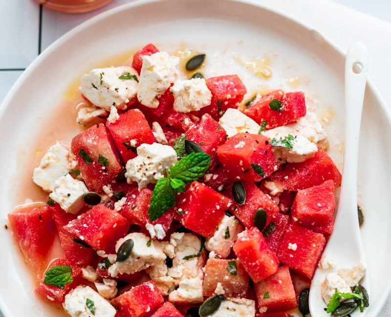 a plate of watermelon and feta salad next to a glass of water