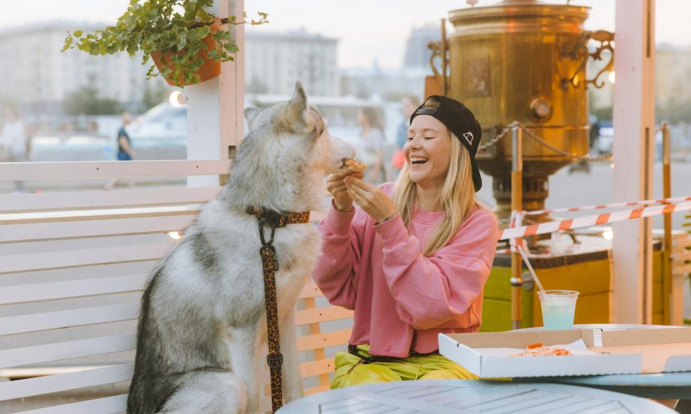A joyful moment of a woman sharing pizza with her husky dog at an outdoor café.
