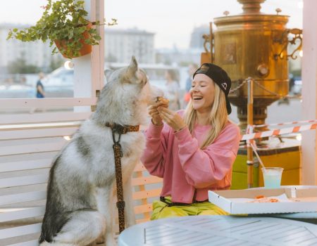 A joyful moment of a woman sharing pizza with her husky dog at an outdoor café.