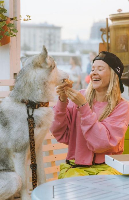 A joyful moment of a woman sharing pizza with her husky dog at an outdoor café.