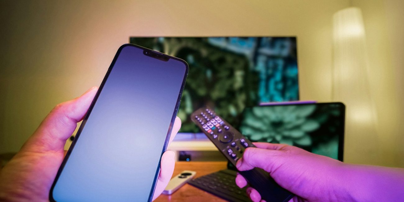 A person holding a cell phone and a remote control