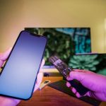 A person holding a cell phone and a remote control