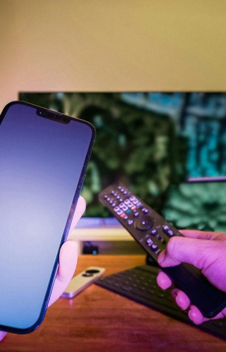 A person holding a cell phone and a remote control