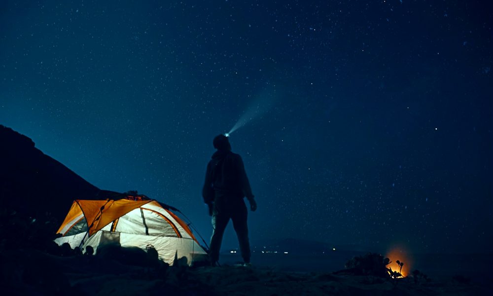 man standing beside camping tent wearing headlamp during nighttime