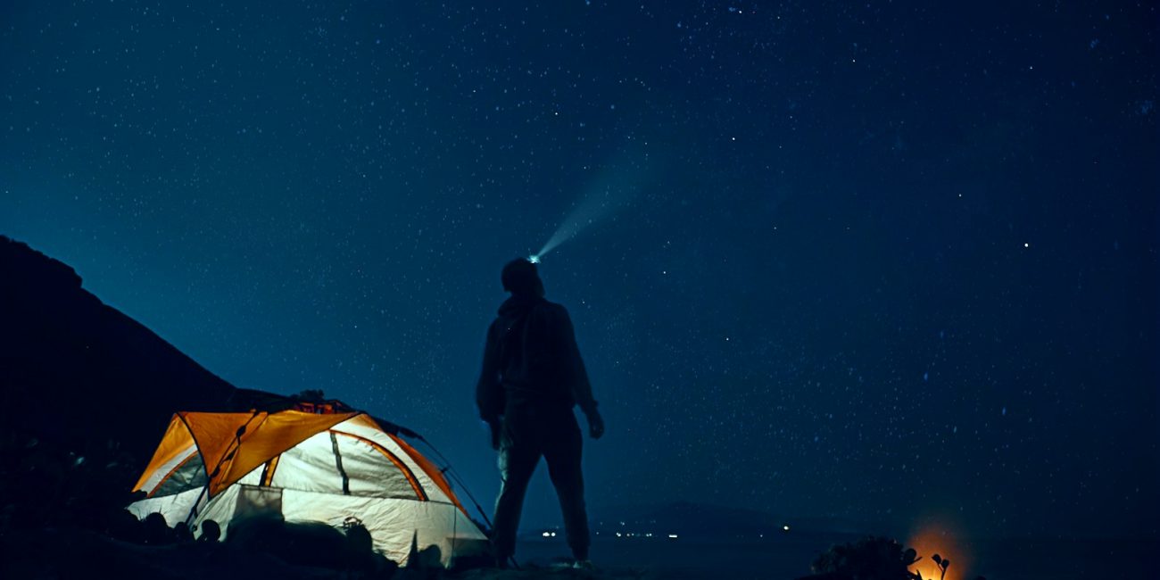 man standing beside camping tent wearing headlamp during nighttime