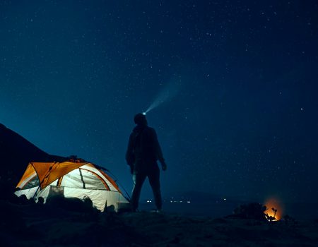 man standing beside camping tent wearing headlamp during nighttime