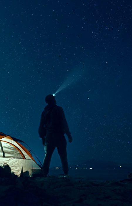 man standing beside camping tent wearing headlamp during nighttime