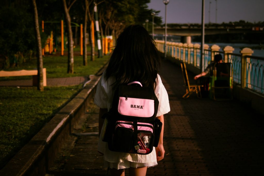 a girl with a pink backpack walking down a sidewalk