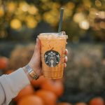a person holding a starbucks drink with oranges in the background