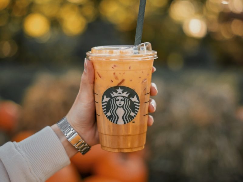 a person holding a starbucks drink with oranges in the background
