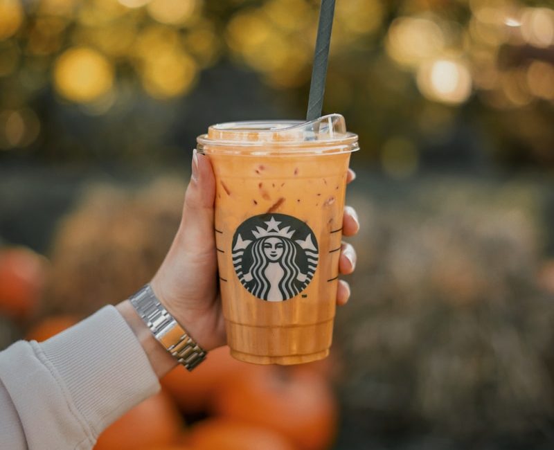 a person holding a starbucks drink with oranges in the background