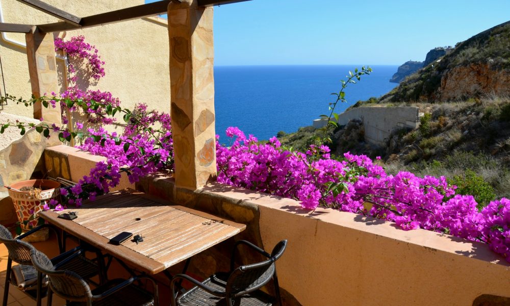 a table and chairs on a balcony with purple flowers