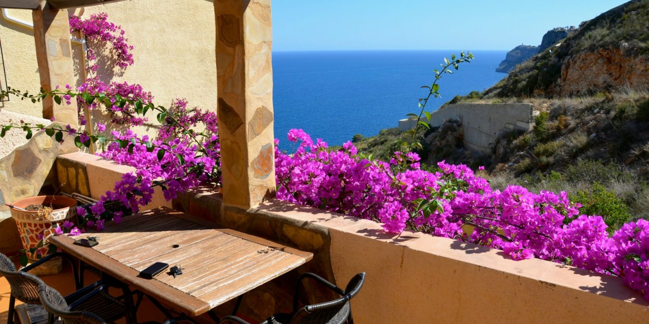 a table and chairs on a balcony with purple flowers