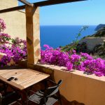 a table and chairs on a balcony with purple flowers