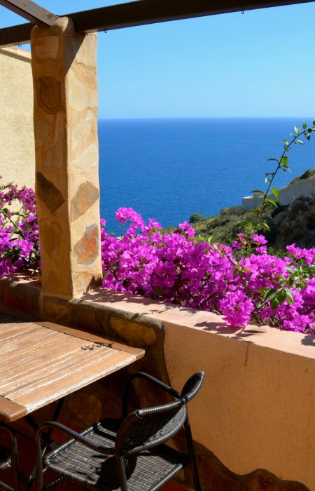 a table and chairs on a balcony with purple flowers