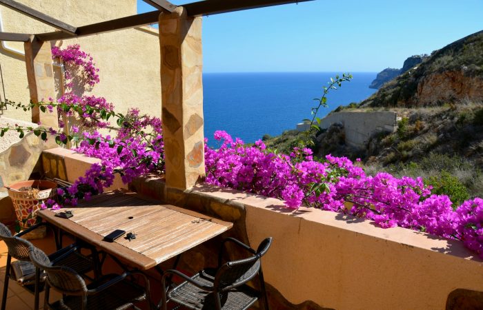a table and chairs on a balcony with purple flowers