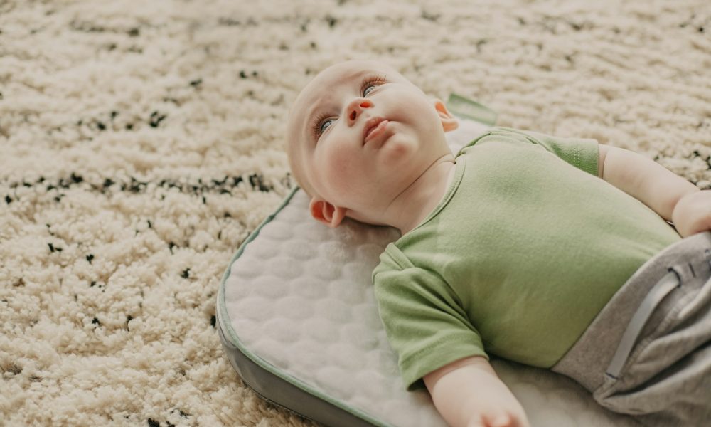 baby in green onesie lying on white and gray bed