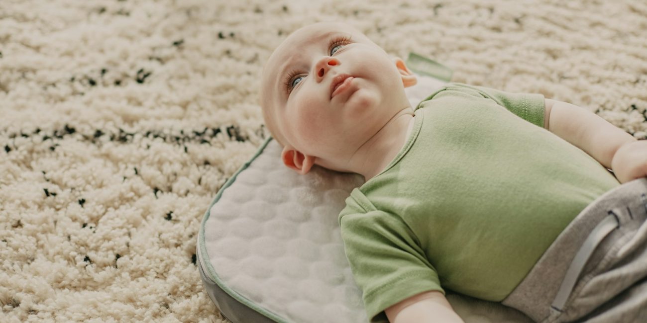 baby in green onesie lying on white and gray bed