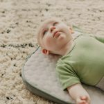 baby in green onesie lying on white and gray bed