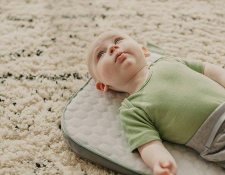 baby in green onesie lying on white and gray bed