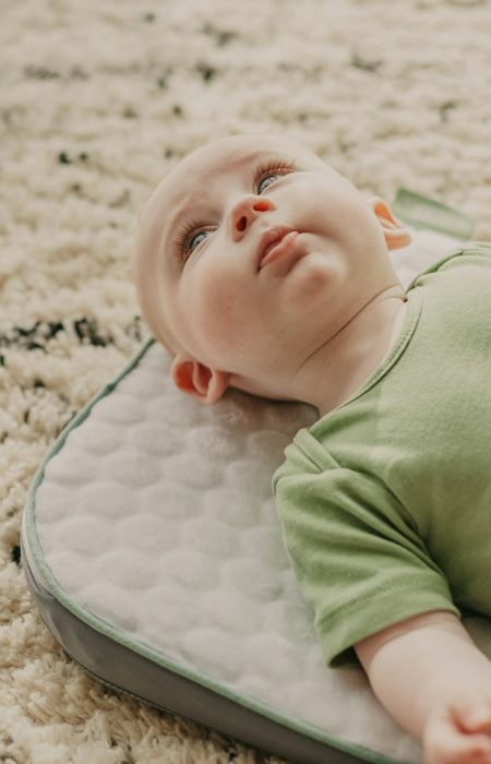 baby in green onesie lying on white and gray bed