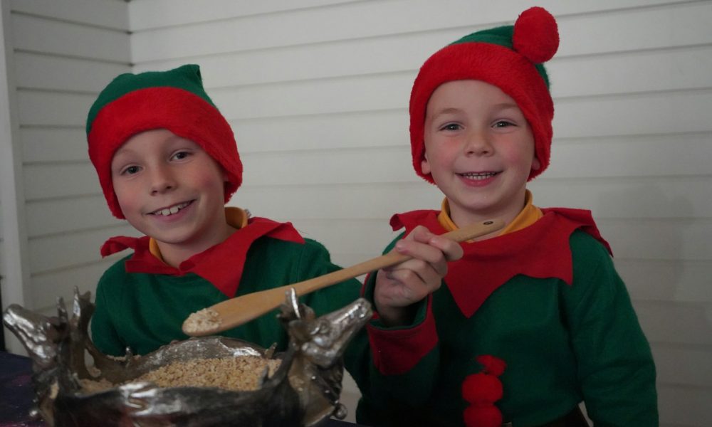 Two elf kids smile while baking.