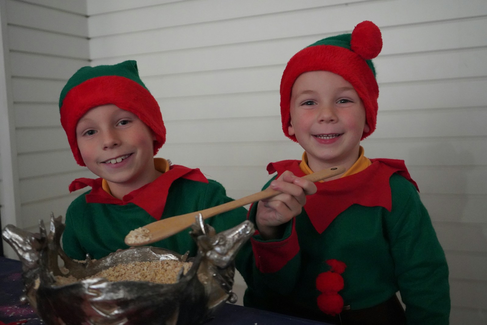 Two elf kids smile while baking.
