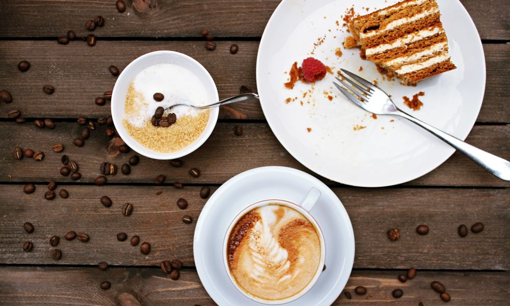 slice of cake on plate beside cappuccino