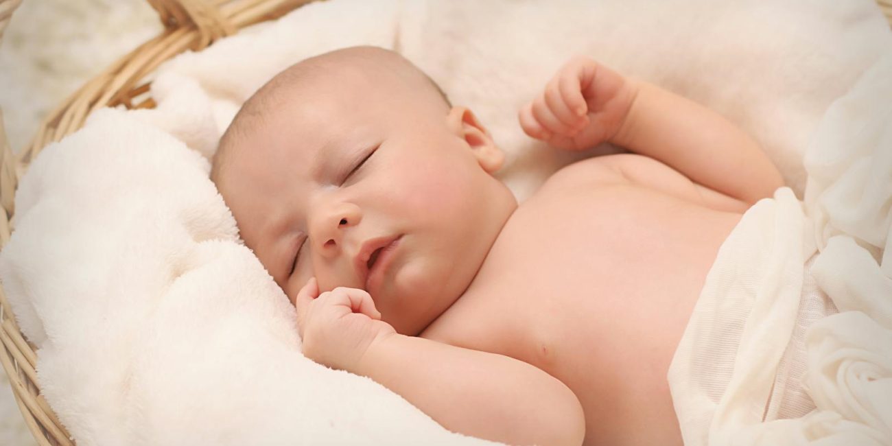 A peaceful sleeping baby nestled in a soft, fluffy blanket inside a wicker basket.